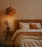 Rust/Stone red-colored sculptural foam pendant light with wavy design hanging over a warm-toned bedroom.
