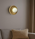 Modern gold wall sconce with circular backplate and soft ambient glow