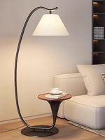 Curved metal floor lamp with fabric shade and round wooden side table