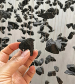 Hand holding a small black stone with a background of similar stones hanging from strings.
