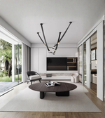 Modern living room with a large round wooden coffee table, stylish armchair, and sleek chandelier.