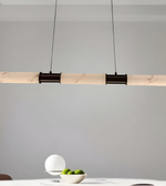 Modern pendant light fixture hanging above a table with a bowl of apples against a gray wall.
