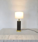 Table lamp with a textured black base and gold accents on a light wooden surface.