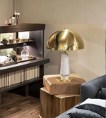 Gold table lamp on a wooden side table with a shelf in the background