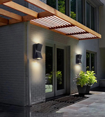 Modern outdoor setting with a wooden pergola, wall lights, and plants.