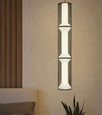 Modern pendant light hanging against a beige wall with a plant and part of a bed visible.