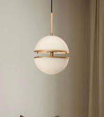 Modern pendant light with white glass shade and gold metal frame against a neutral wall.