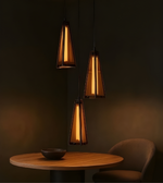 Three pendant lights hanging above a table with a bowl and chair in a dimly lit room.