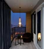 Modern balcony with a chair, small table, and pendant light overlooking a cityscape at night.
