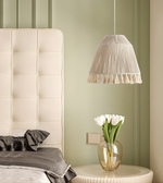 Neatly made bed with a white upholstered headboard, gray bedding, and a small table with a vase of white tulips against a green wall.