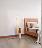 Leaf-shaped gold floor lamp with marble base beside a wooden bed
