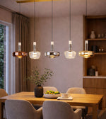 modern multi glass pendant lights in mixed finishes hanging above dining table, warm ambient lighting