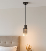 Modern smoked glass cylinder pendant light hanging beside bed creating warm ambient lighting in contemporary bedroom