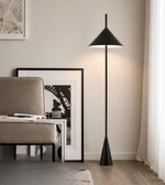 Modern black floor lamp in a room with a sofa and framed picture on the wall.