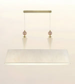 A modern rectangular pendant light fixture with a large white textured drum shade, a brushed brass canopy, and two hanging rose gold beads.