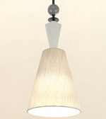 A modern pendant light with a textured beige pleated shade, a white geometric neck, and a dark gray suspension rod against a warm off-white background.