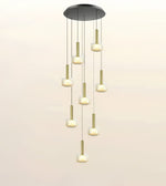 A modern multi-light linear pendant chandelier with a circular black ceiling canopy, gold-toned vertical rods, and frosted cylindrical glass shades that glow with warm light, shown against a plain off-white background.