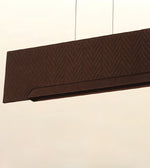 A close-up of a dark brown rectangular pendant light fixture with a textured chevron pattern, suspended by thin cables against a plain off-white background.