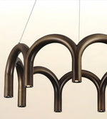 A modern multi-arm chandelier with a dark bronze metallic finish, suspended by thin cables against a light beige background.