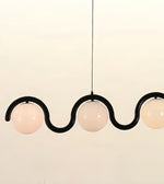A modern three-light linear pendant chandelier with a black wavy metal frame and frosted white glass globes, suspended against a plain off-white background.
