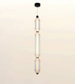 A modern multi-light linear pendant ceiling fixture with three illuminated glass cylindrical bulbs suspended vertically from a black ceiling canopy.