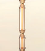 A close-up of a decorative hanging light fixture with clear cylindrical glass shades and warm metallic rose-gold or copper-toned accents, shown against a soft cream background.