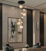 Modern multi-light pendant chandelier with multiple spherical frosted glass shades hanging in staggered rows from a black ceiling canopy, shown in a contemporary interior lobby with seating and wall art.