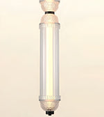 A modern cylindrical pendant light fixture with a ribbed clear glass shade and textured glass caps, glowing with a warm light against a plain beige background.