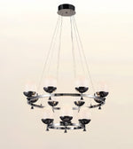 A modern multi-light chandelier with a polished silver-tone metal frame, featuring multiple frosted glass shades and dark metal cup holders, suspended from a circular ceiling canopy against a plain light background.