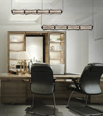 Modern office interior featuring two black leather chairs in the foreground, a wooden desk and shelving unit, and two long rectangular pendant lights hanging from the ceiling.