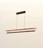 A modern linear LED pendant light with a dark wood frame and a curved, translucent white diffuser, suspended from a matching dark wood ceiling canopy against a plain, light beige wall.