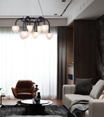 Modern multi-light chandelier with frosted glass globe shades and a black metal frame, hanging in a contemporary living room with a sofa, armchair, and large window.