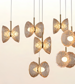 A set of modern pendant lights with faceted, butterfly-like clear glass shades and warm gold metal accents, shown hanging against a plain light background.