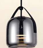 A modern pendant light with a glossy, dark smoky glass dome shade and black hanging straps, shown against a solid light beige background.