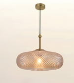 A modern pendant light with a textured, diamond-patterned glass shade in a warm frosted pink-tinted glass, suspended by a brass rod and canopy against a plain off-white background.