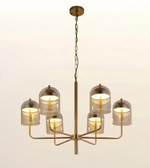 A modern six-light brass chandelier with clear glass dome shades, suspended from a central rod by a chain against a plain light background.