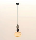 A modern pendant light fixture with a black ceiling canopy and cord, featuring stacked glass and stone-like elements including a smoky gray oval piece, a black sphere, and a warm beige marbled teardrop shade at the bottom.