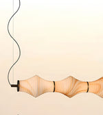 A modern pendant light with a ribbed, translucent beige shade that glows warm white, suspended by a black cord against a pale cream background.