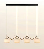A modern 4-light linear pendant chandelier with a matte black top bar and arms, and warm white frosted glass shades, shown against a light beige gradient background.