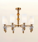 A modern six-light chandelier with a brushed gold metal frame, clear glass crystal accents, and white cylindrical fabric shades, shown against a plain light beige background.