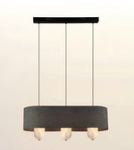 A modern three-light linear pendant chandelier with a dark gray fabric drum shade, a black ceiling canopy, and three marble-style glass globes, shown against a light beige gradient background.