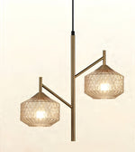 A modern two-light pendant lamp with a brushed brass/gold central pole and arms, featuring faceted clear glass shades that glow with warm light, shown against a plain off-white background.