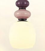 A modern pendant light fixture with a three-tiered stacked glass design. The top two tiers are in frosted dusty purple and dusty pink glass, while the large bottom tier is a warm, glowing frosted white glass shade.