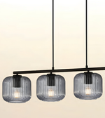 Three-light linear pendant chandelier with ribbed clear glass shades and a black metal frame, shown against a warm off-white background.