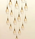 A modern multi-light linear chandelier with multiple clear glass pendant bulbs wrapped in a twisted spiral, suspended by thin cords against a warm beige background.