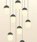 Modern multi-light pendant chandelier with matte black acorn-shaped caps and frosted white cylindrical shades hanging at varying lengths against a warm off-white background.
