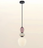A modern multi-tier pendant light fixture with a black metal rod, a dusty pink glass bulb, a textured white glass bulb, and a ribbed white glass shade, shown against a plain off-white background.