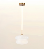 A modern pendant light fixture with a brushed gold ceiling canopy and downrod, a black cord, and a frosted white glass shade, shown against a soft beige gradient background.