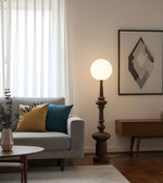 Wooden finish sculptural floor lamp with opal globe beside sofa in living room