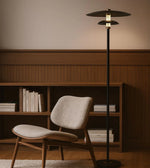 Modern floor lamp next to a chair and bookshelf in a room with wooden paneling.